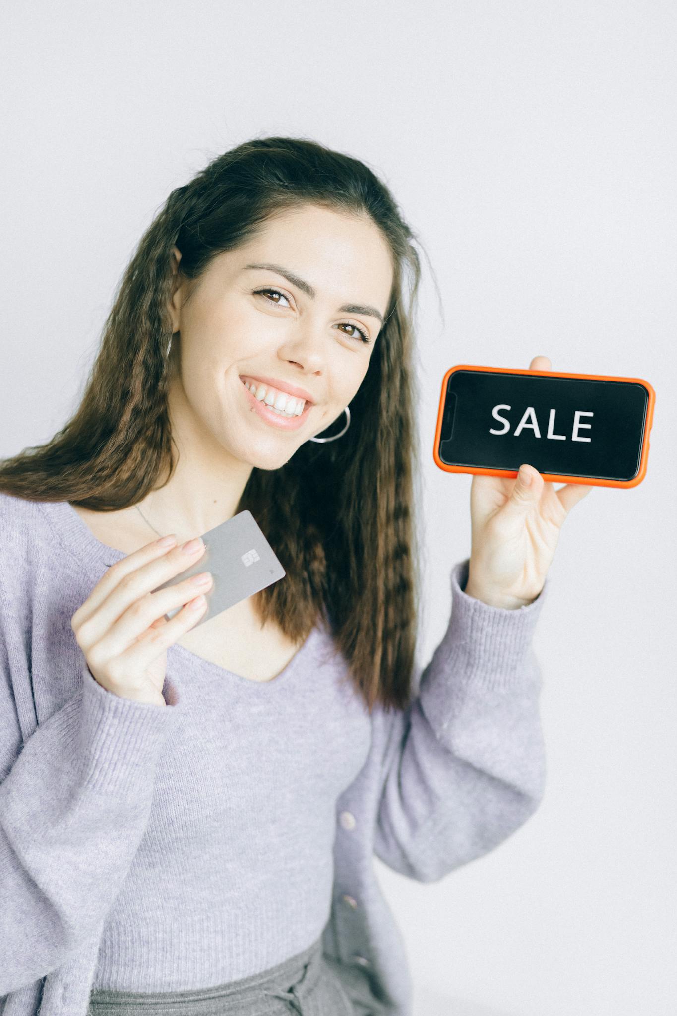 Happy woman promoting online shopping with credit card and sale sign.
