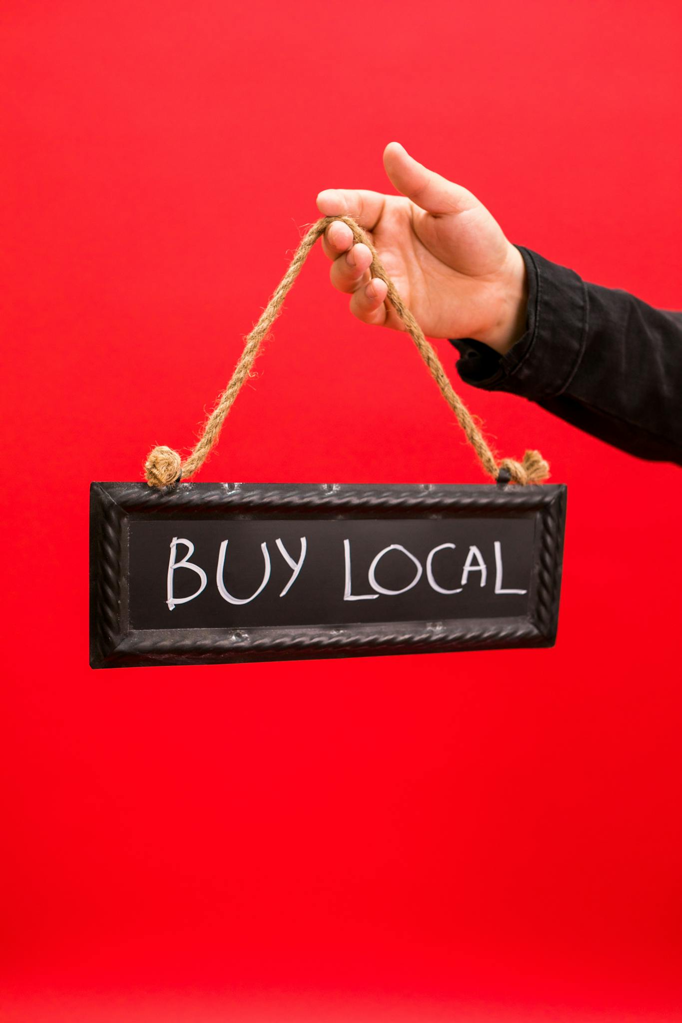 Person holding a 'Buy Local' sign suspended on ropes, promoting local business.